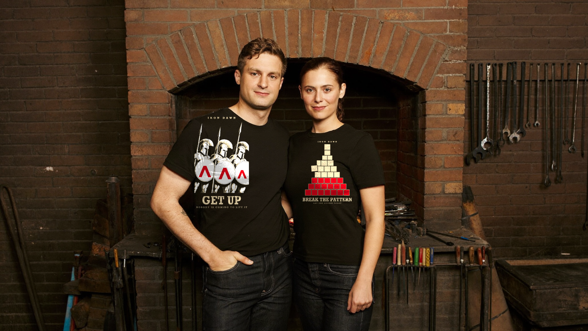Two people in black Iron Dawn tees in a blacksmith's forge