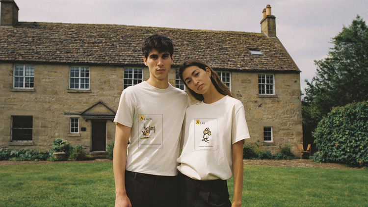 Two people in cream Ye Olde Grievances tees on a village green