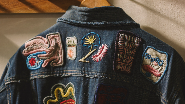 Embroidered patches sewn across the back of a worn denim jacket