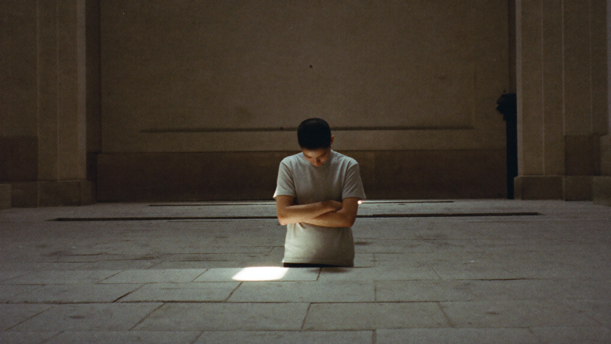 A lone figure kneeling in a shaft of light in a vast stone chapel