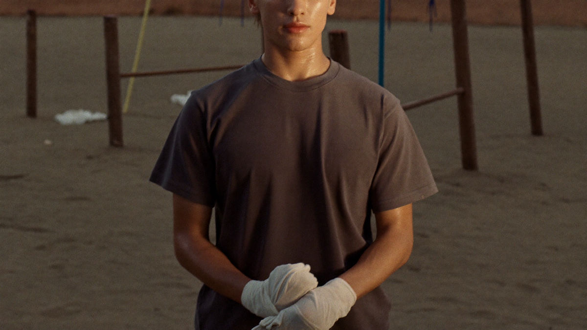 A fighter with wrapped hands in a bare sand training yard at dusk