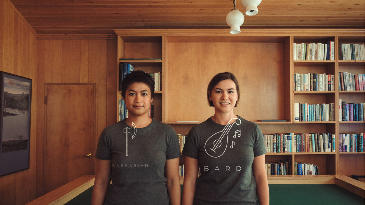 Two people in charcoal class icon tees in a wood panelled library