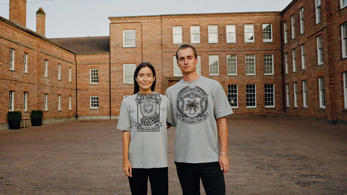 Two people in ash grey guild crest tees in a brick college courtyard