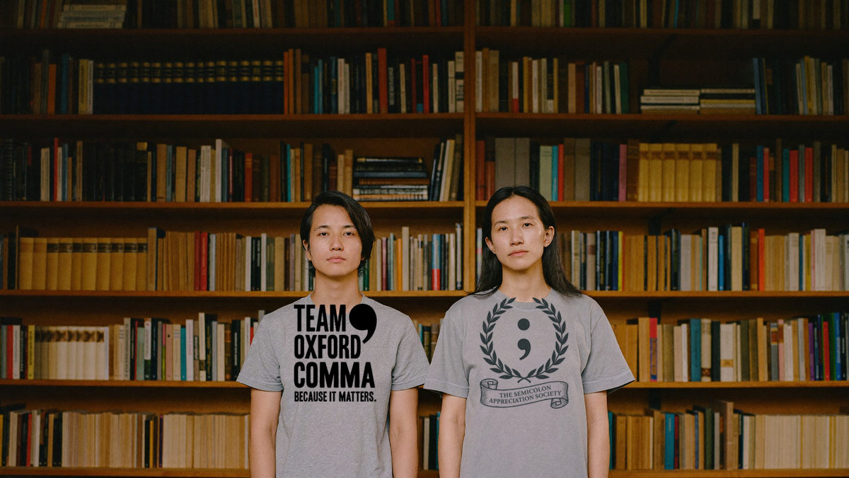 Two people in grey grammar tees in front of full bookshelves